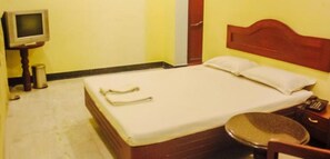 A small, simple room with a bed, a small table, and a television. - Krishna Park (Chennai)