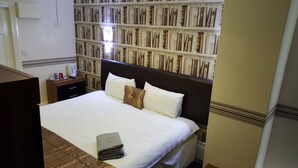Habitación de hotel con una cama grande, una mesita de noche, un armario y una pared con papel tapiz estampado.