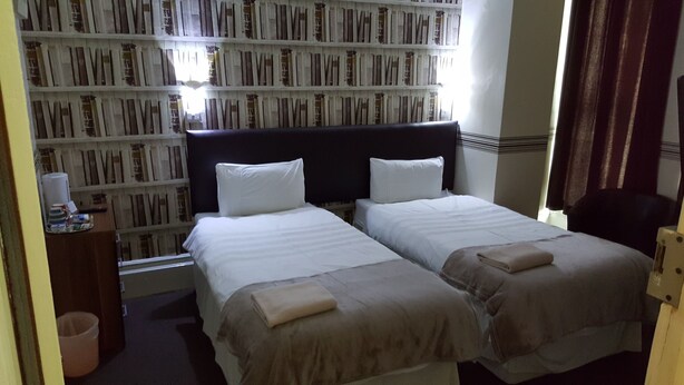 Habitación de hotel con dos camas, una estantería, un escritorio con lámpara y una ventana con cortinas.