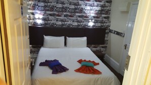 Una habitación de hotel con una cama, almohadas blancas, un cabecero y una pared decorada con imágenes históricas.