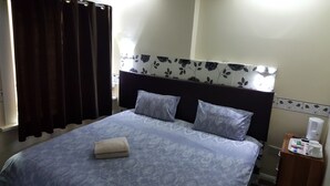 Una habitación de hotel con una cama, una mesita de noche, una ventana con cortinas y una pared con estampado floral.