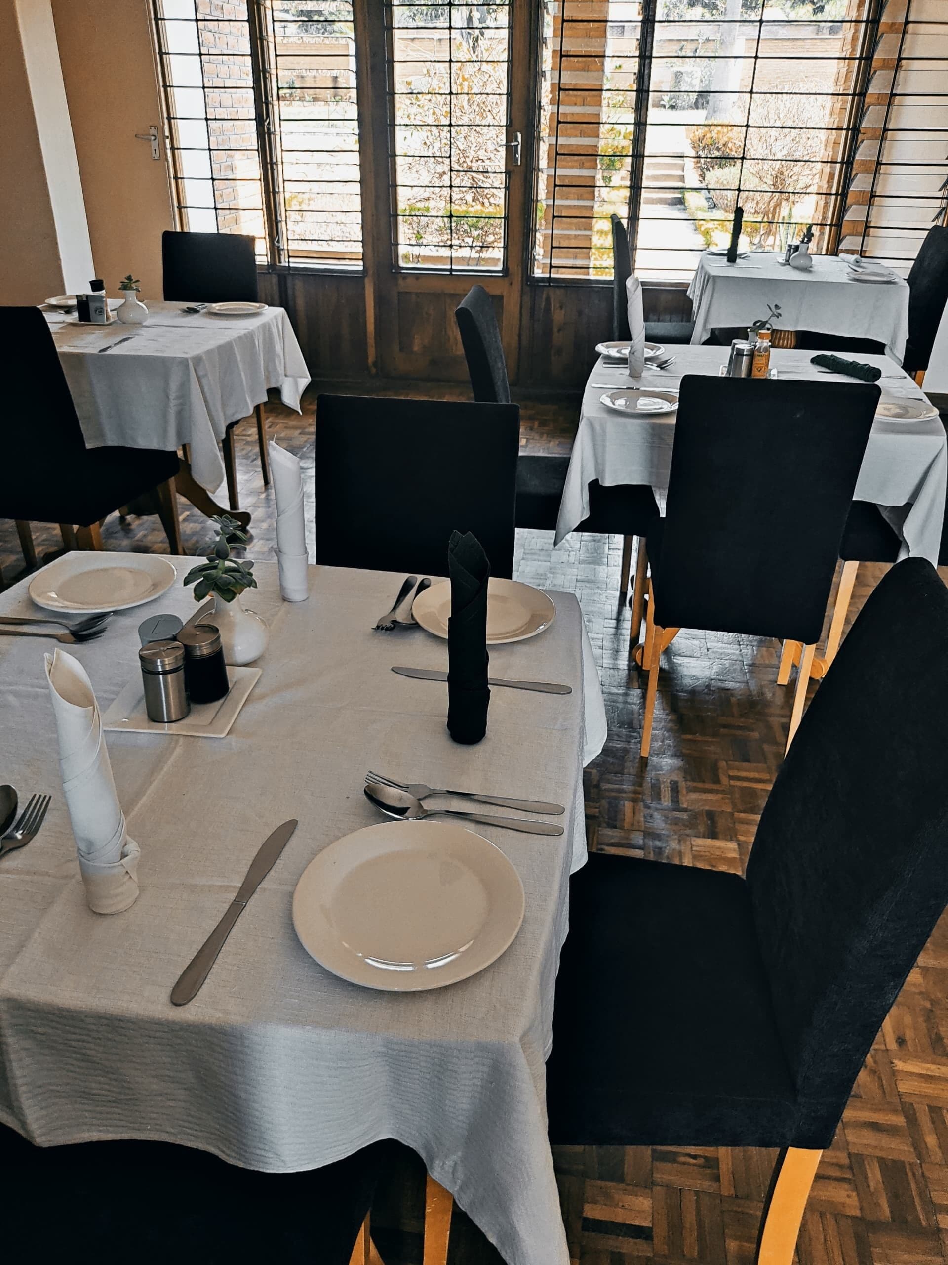 A restaurant with tables set for dining, featuring a view through large windows.
