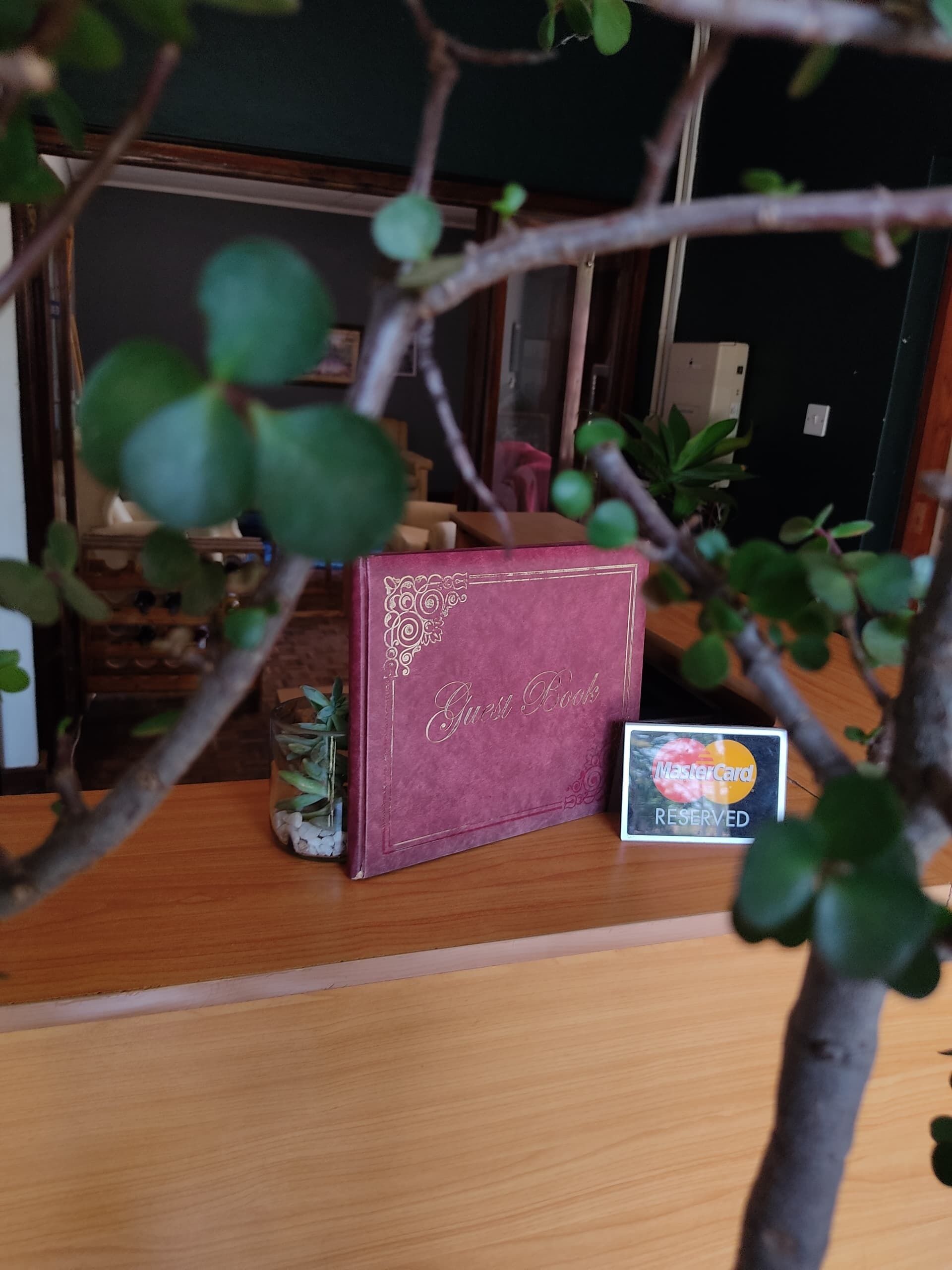 A wooden table with a guest book, a glass container with plants, and a reserved MasterCard sign.