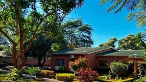 Una casa residencial con un césped cuidado, fachada de ladrillo y diversos árboles y arbustos.