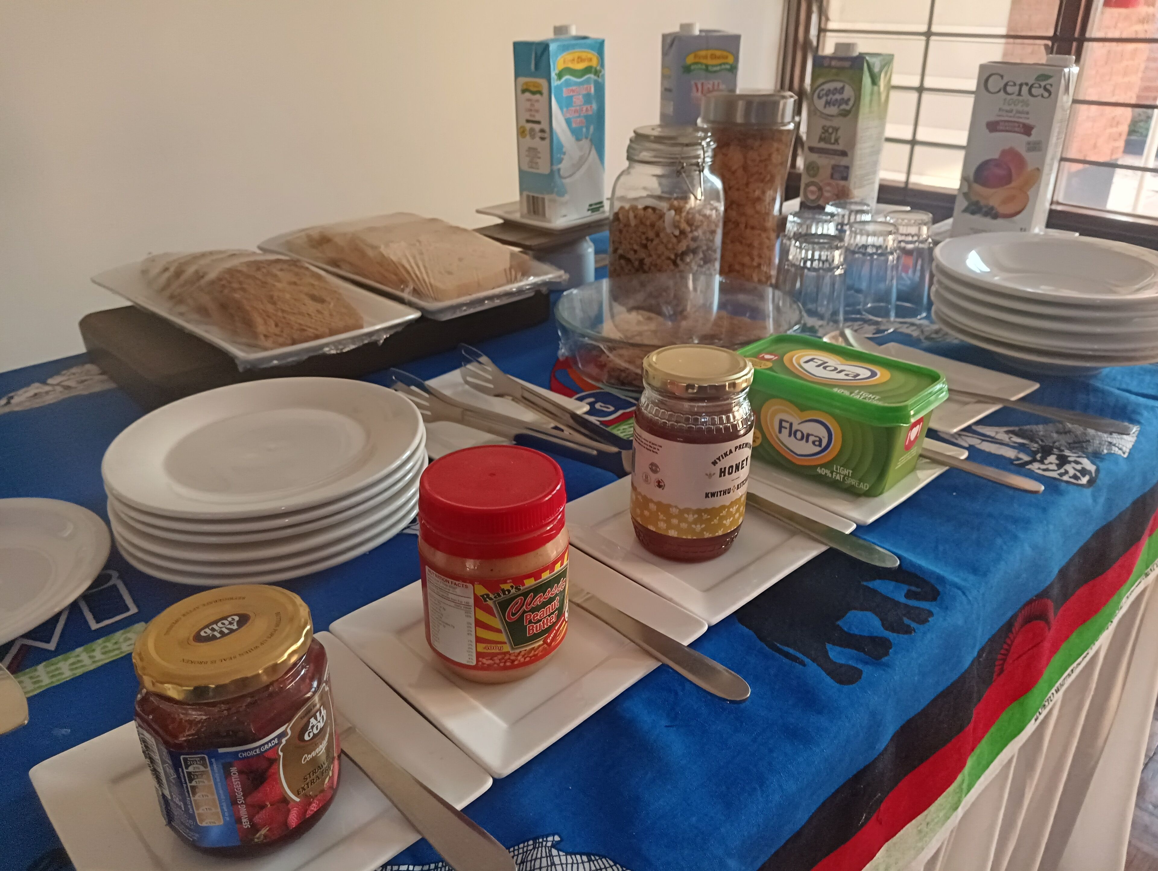 A buffet table with various food items and condiments, including jars of honey and peanut butter, and containers of cereal and milk.