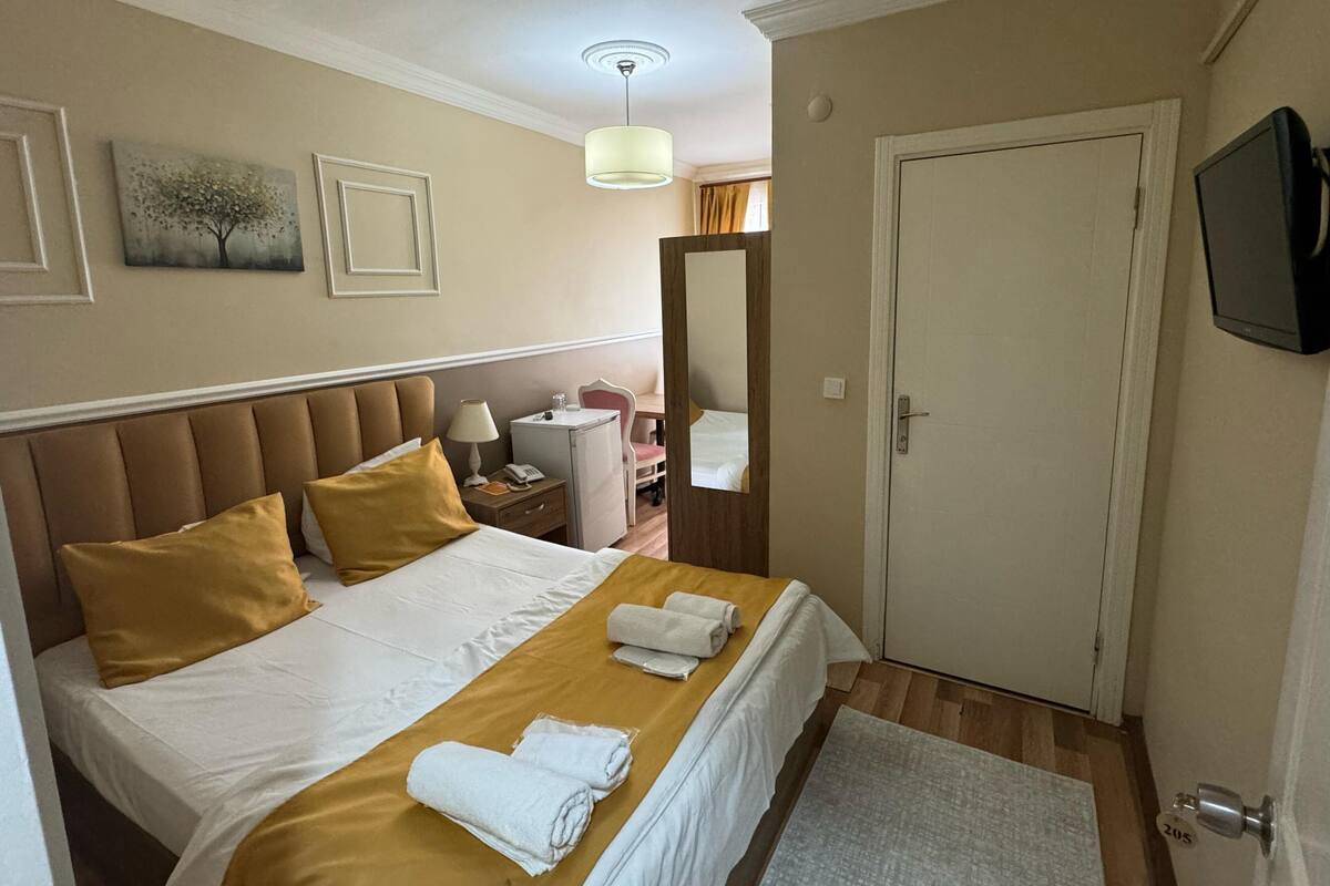Et hotelværelse med seng, natbord, lampe og et fjernsyn ophængt på væggen.