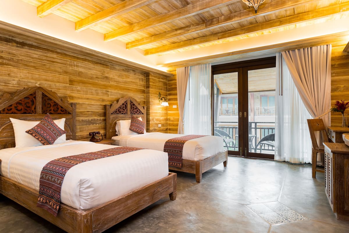 Una habitación con dos camas de madera, techo de madera y un balcón con vistas.