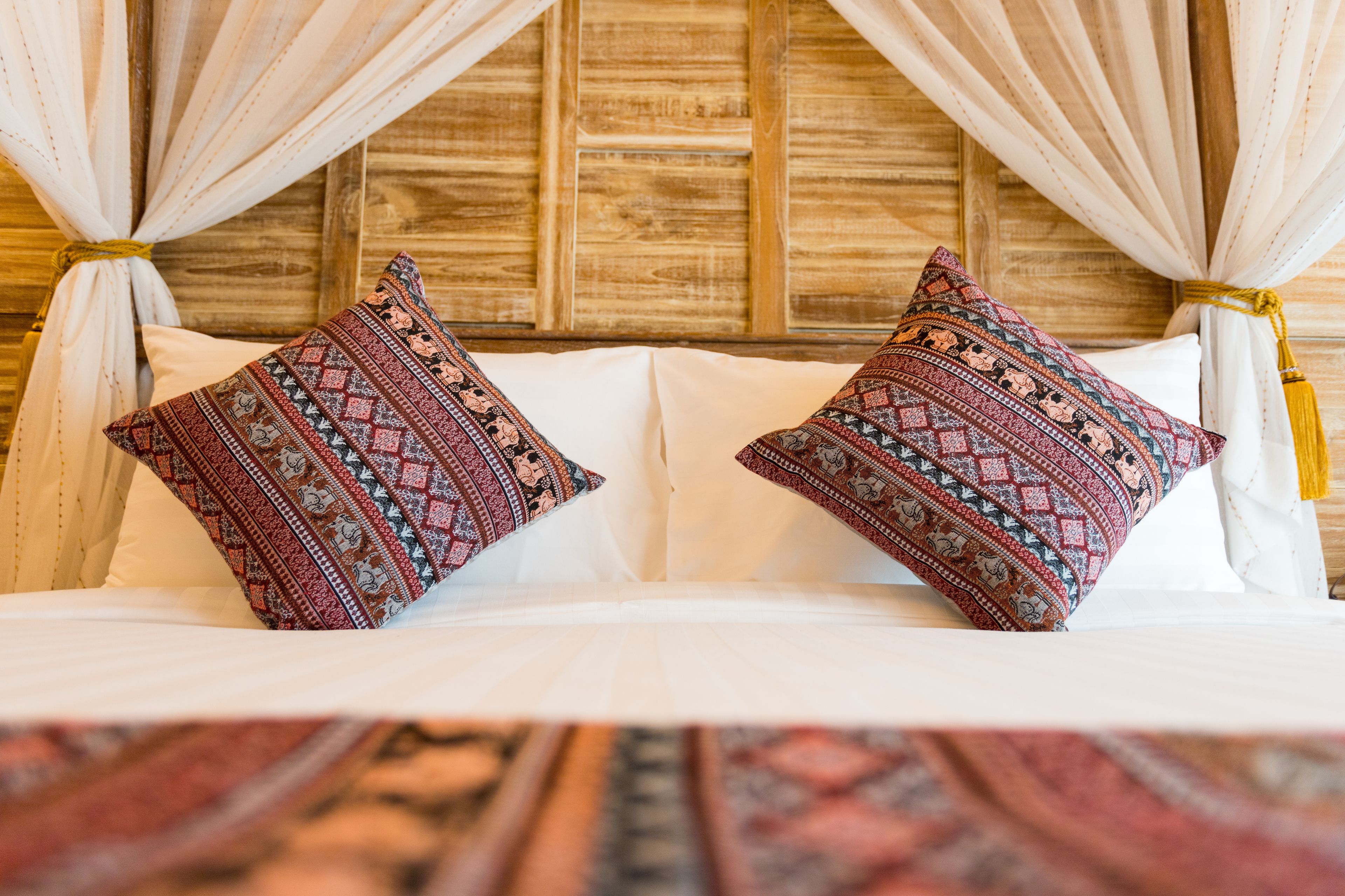 A bed with white linens and two decorative pillows with intricate patterns.