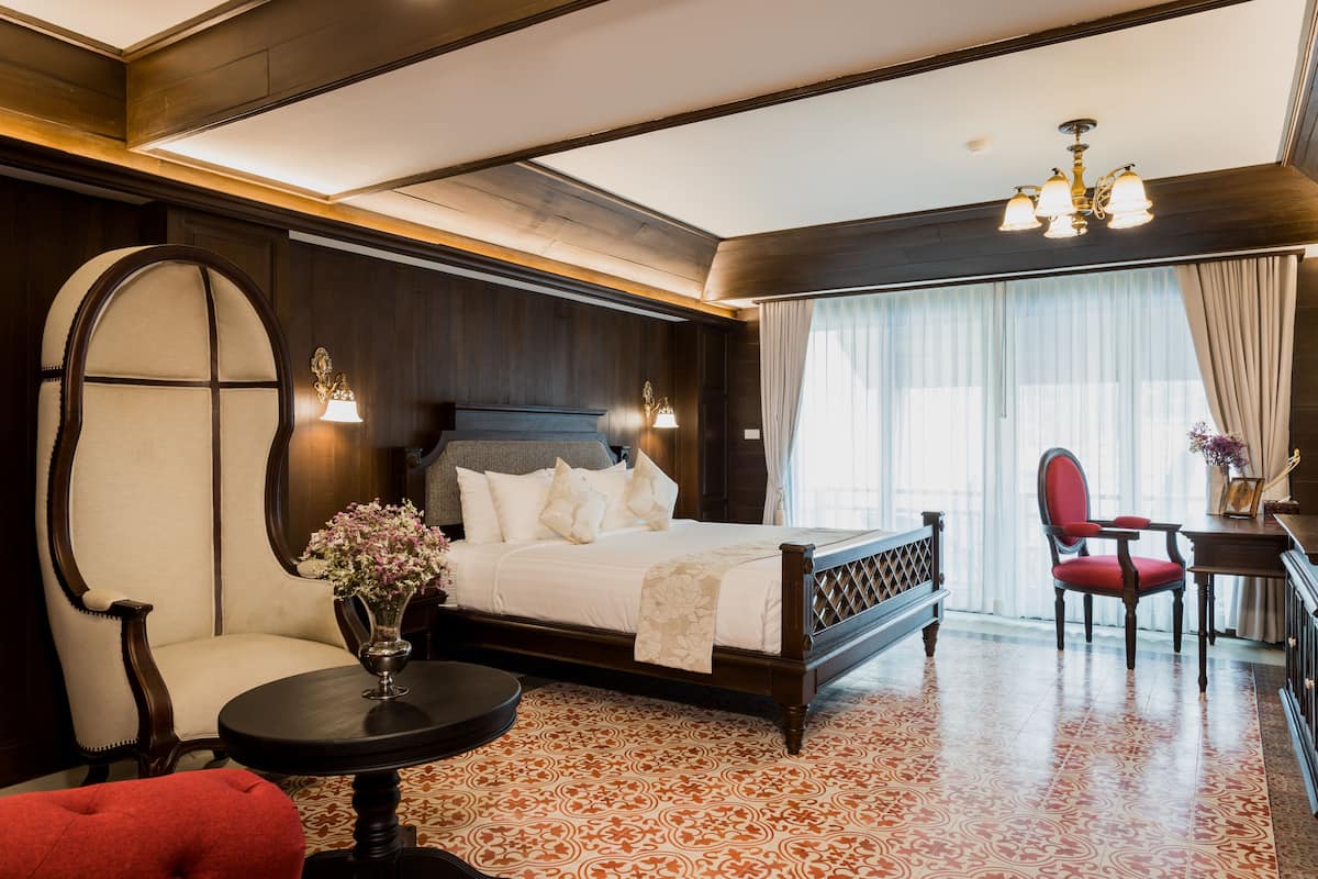 Una habitación de hotel elegante con una cama grande, un espacio de descanso con una silla y una mesa, y un escritorio con una silla.