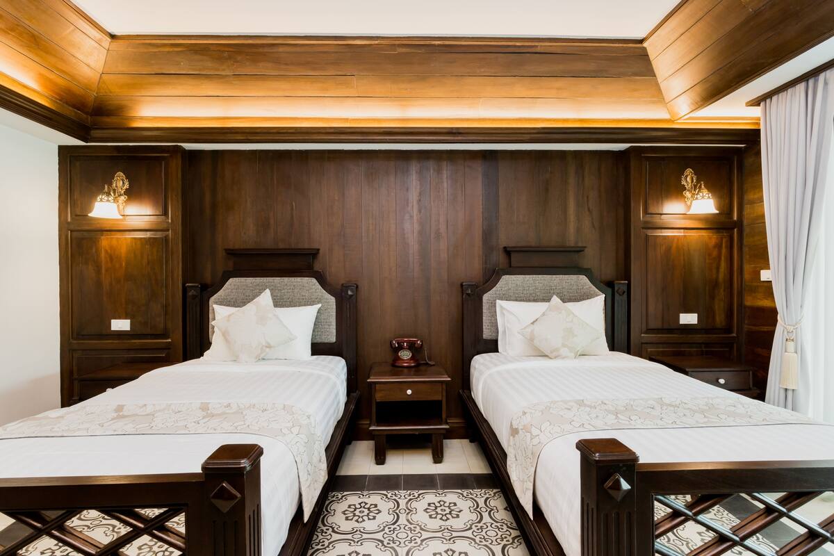 Habitación doble con dos camas, cabeceros de madera, mesitas de noche con lámparas y suelo estampado.