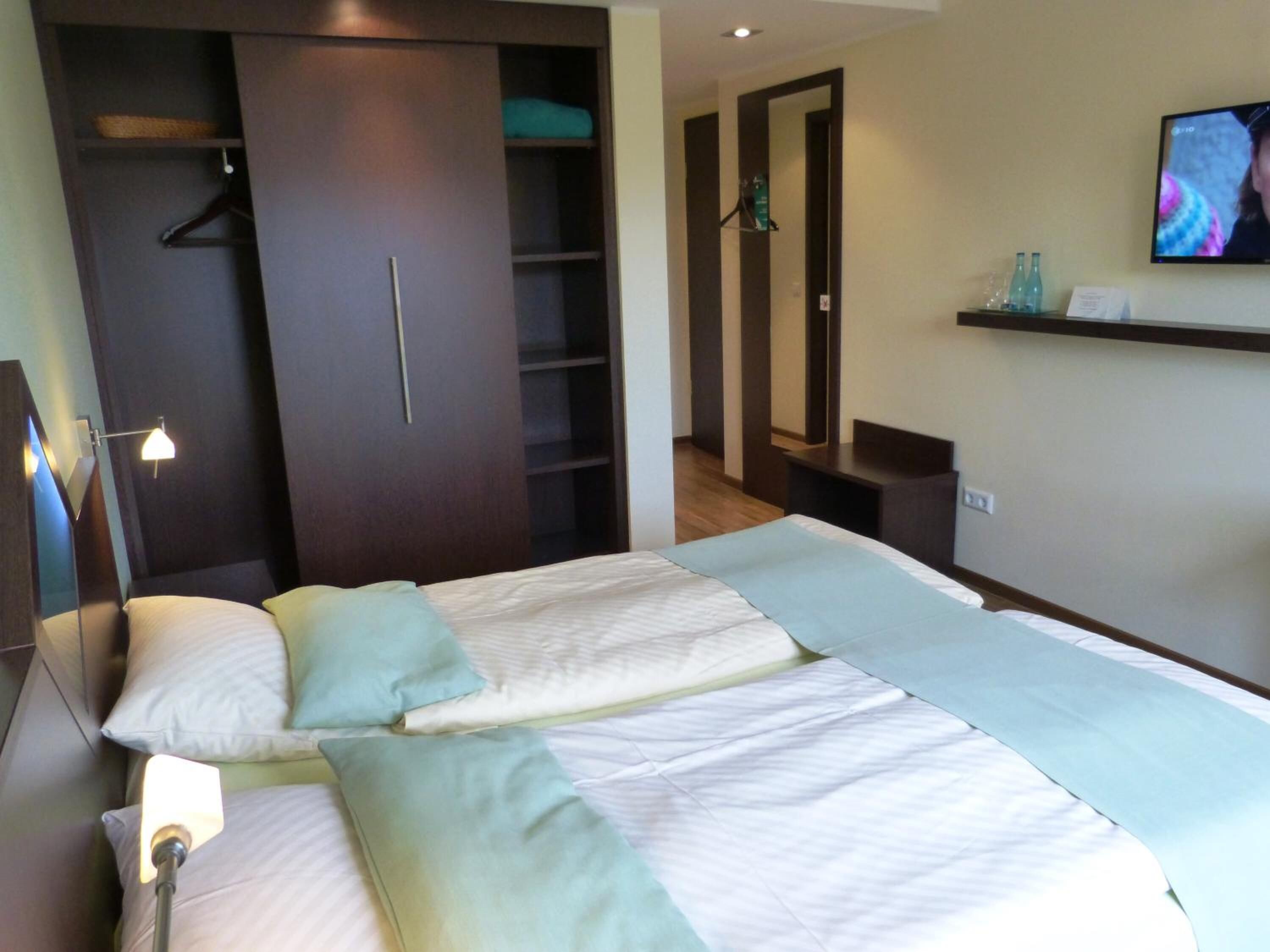 Ein Hotelzimmer mit Bett, Schrank, Fernseher und einer Ablage mit Flaschen.