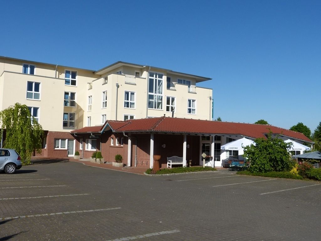 A hotel with a parking lot, a covered area, and a building with multiple windows and a red roof.