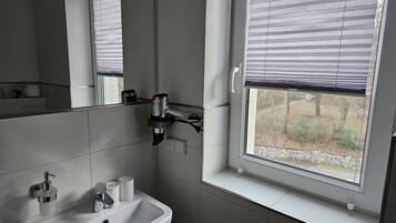 A bathroom with a sink, mirror, and window with blinds.