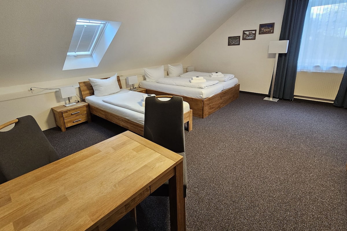 Ein Hotelzimmer mit zwei Betten, einem Schreibtisch, einem Stuhl, einem Fenster und einem kleinen Tisch.