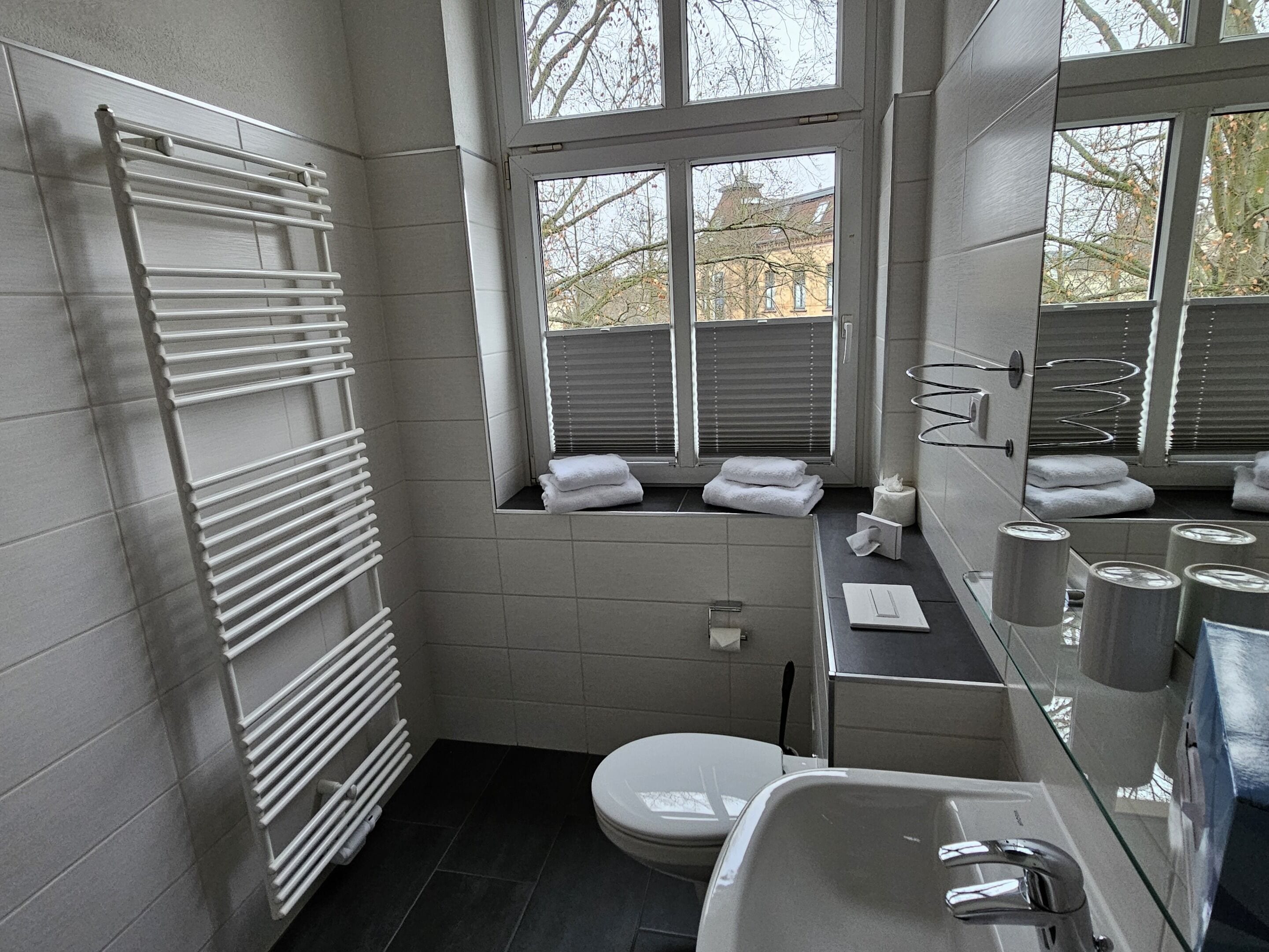 Een moderne badkamer met een witte badkuip, toilet, wastafel en een raam met uitzicht op bomen.