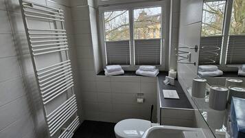 Een moderne badkamer met een witte badkuip, toilet, wastafel en een raam met uitzicht op bomen.
