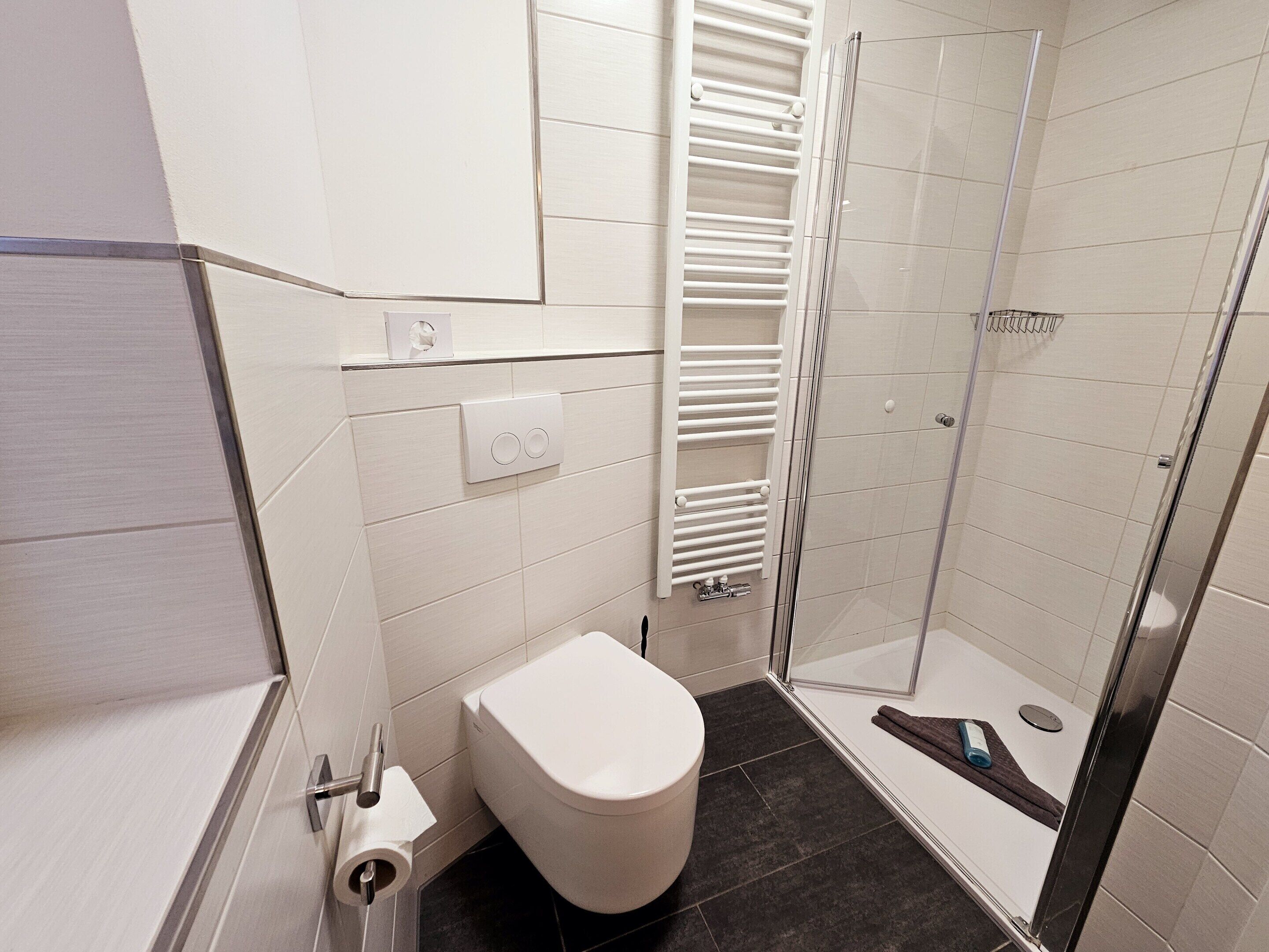 A modern bathroom with a toilet, a shower, and a towel rack.