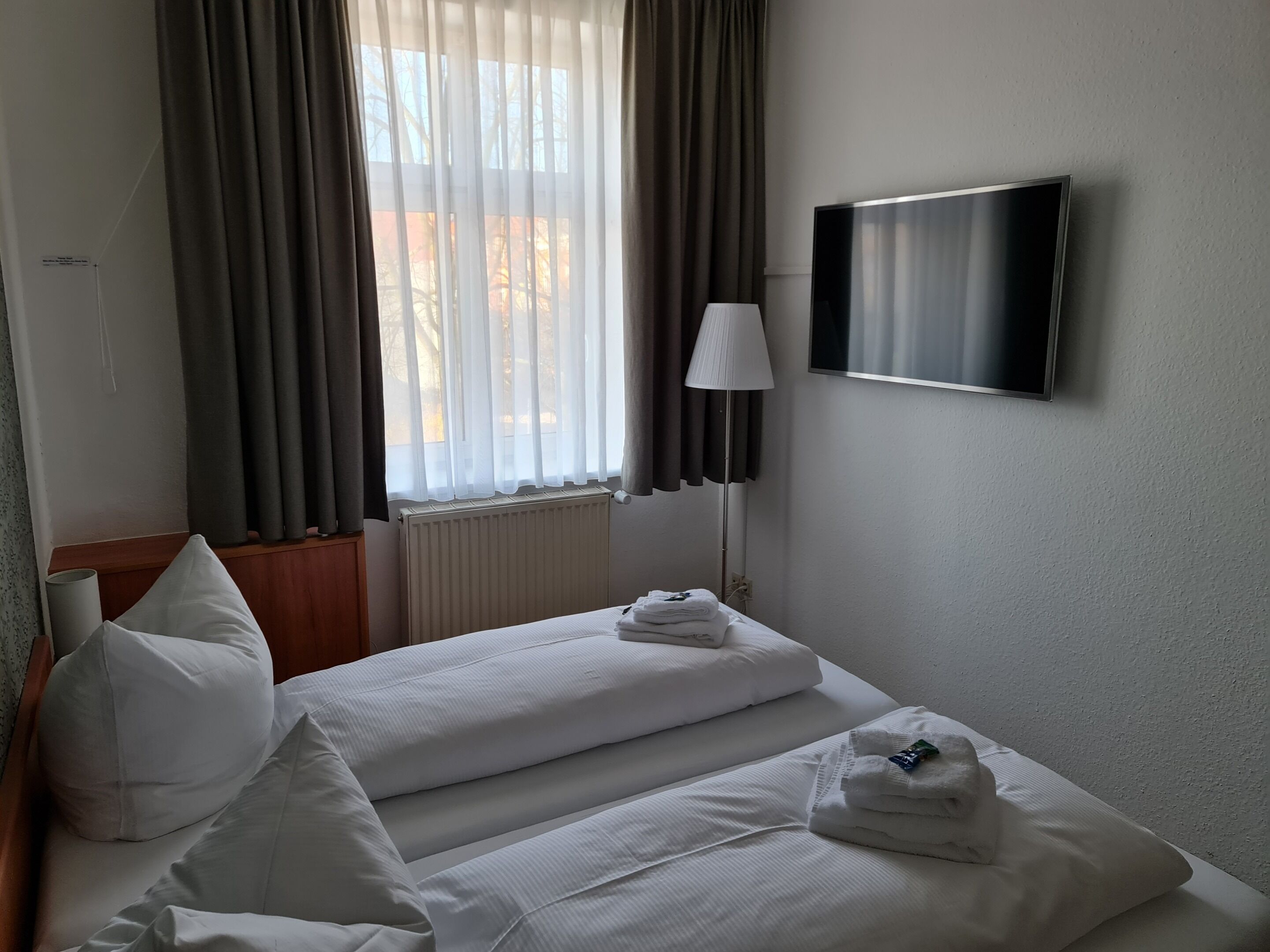 Ein Hotelzimmer mit zwei Betten, einem Fernseher, einer Lampe und einem Fenster mit Vorhängen.