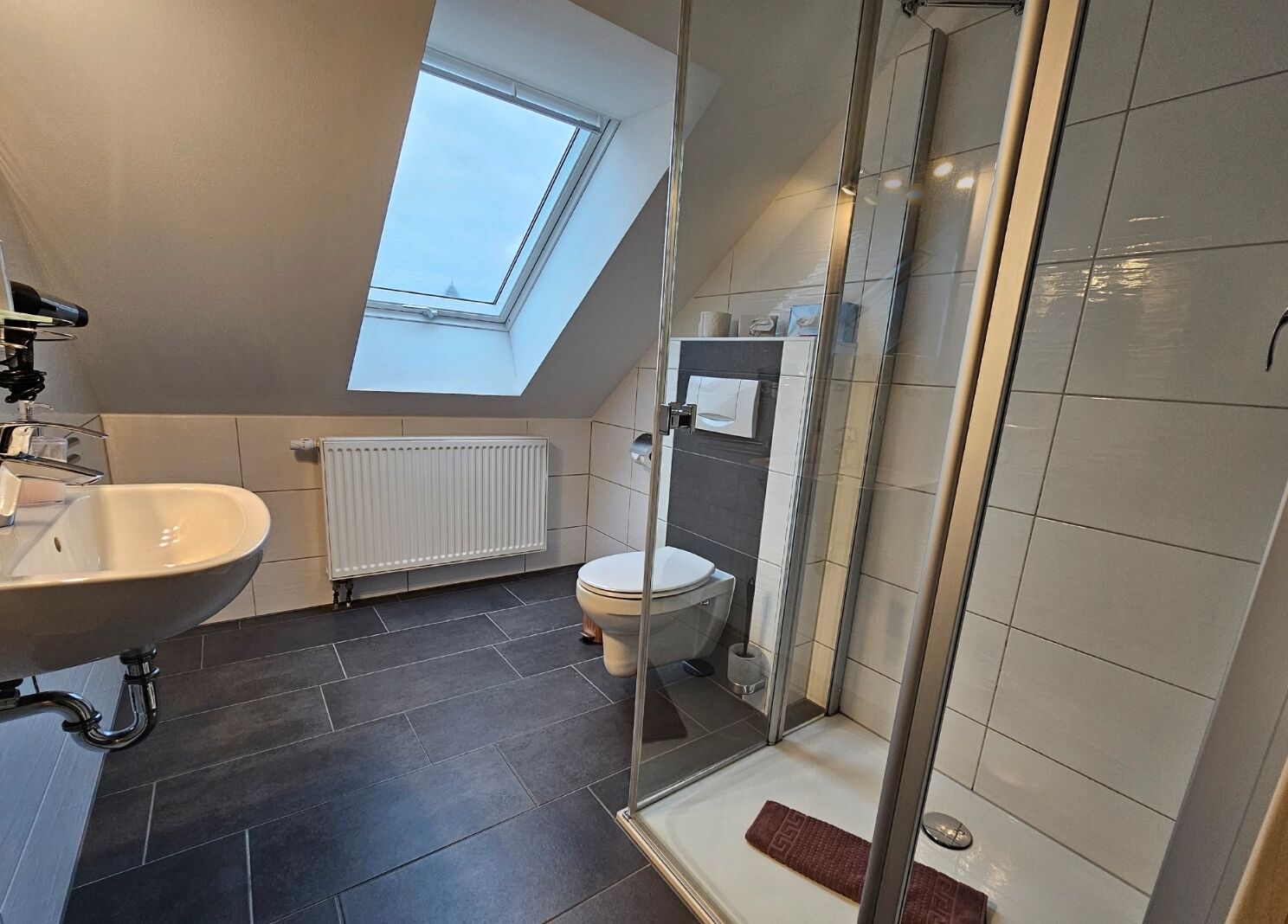 Un baño moderno con tragaluz, bañera independiente, ducha con mampara de vidrio y un inodoro.