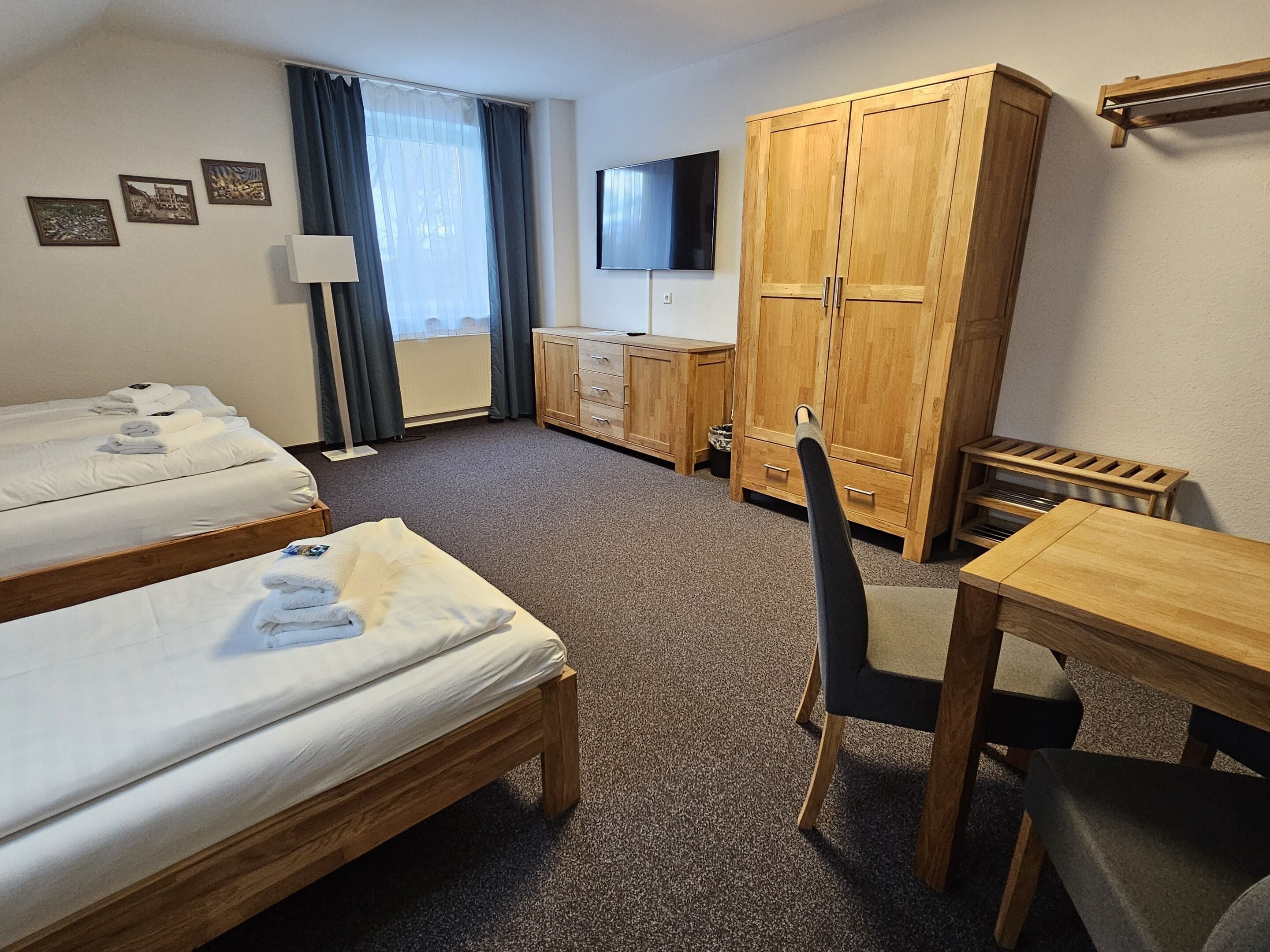 A hotel room with two single beds, a wooden desk, a chair, a wardrobe, and a television on the wall.