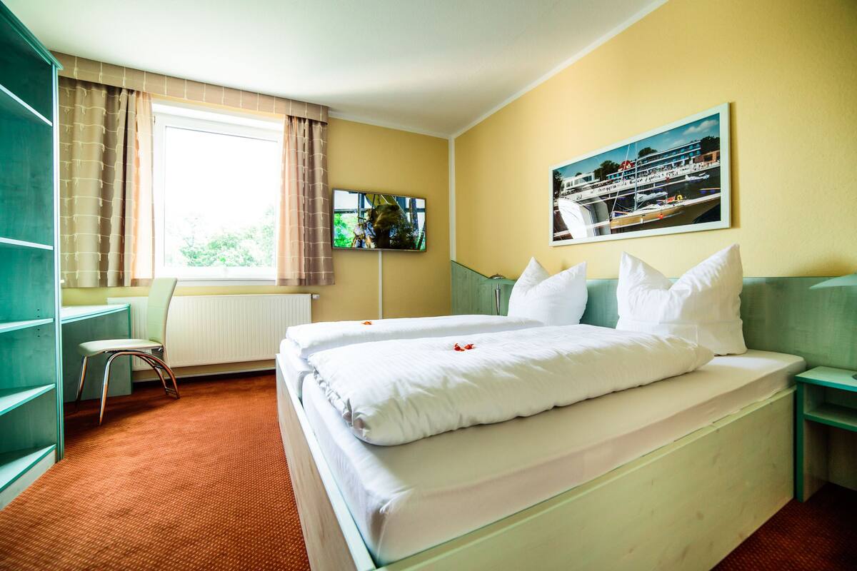 Ein Hotelzimmer mit einem Bett, einem Schreibtisch, einem Stuhl, einem Fernseher und einem fenster mit Vorhängen.