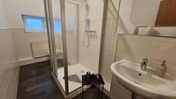Un baño moderno con ducha envuelta en vidrio, un lavamanos blanco y una mesita con artículos de aseo.