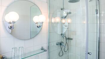 Un baño moderno con cabina de ducha de vidrio, un espejo redondo con apliques de pared y un estante de vidrio con artículos de aseo.