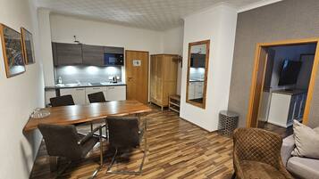 A modern, well-lit room with a wooden dining table, chairs, a sofa, and a TV.