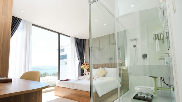 Habitación de hotel moderna con una cama grande, cabina de ducha de vidrio, zona de comedor con mesa y vistas al mar.