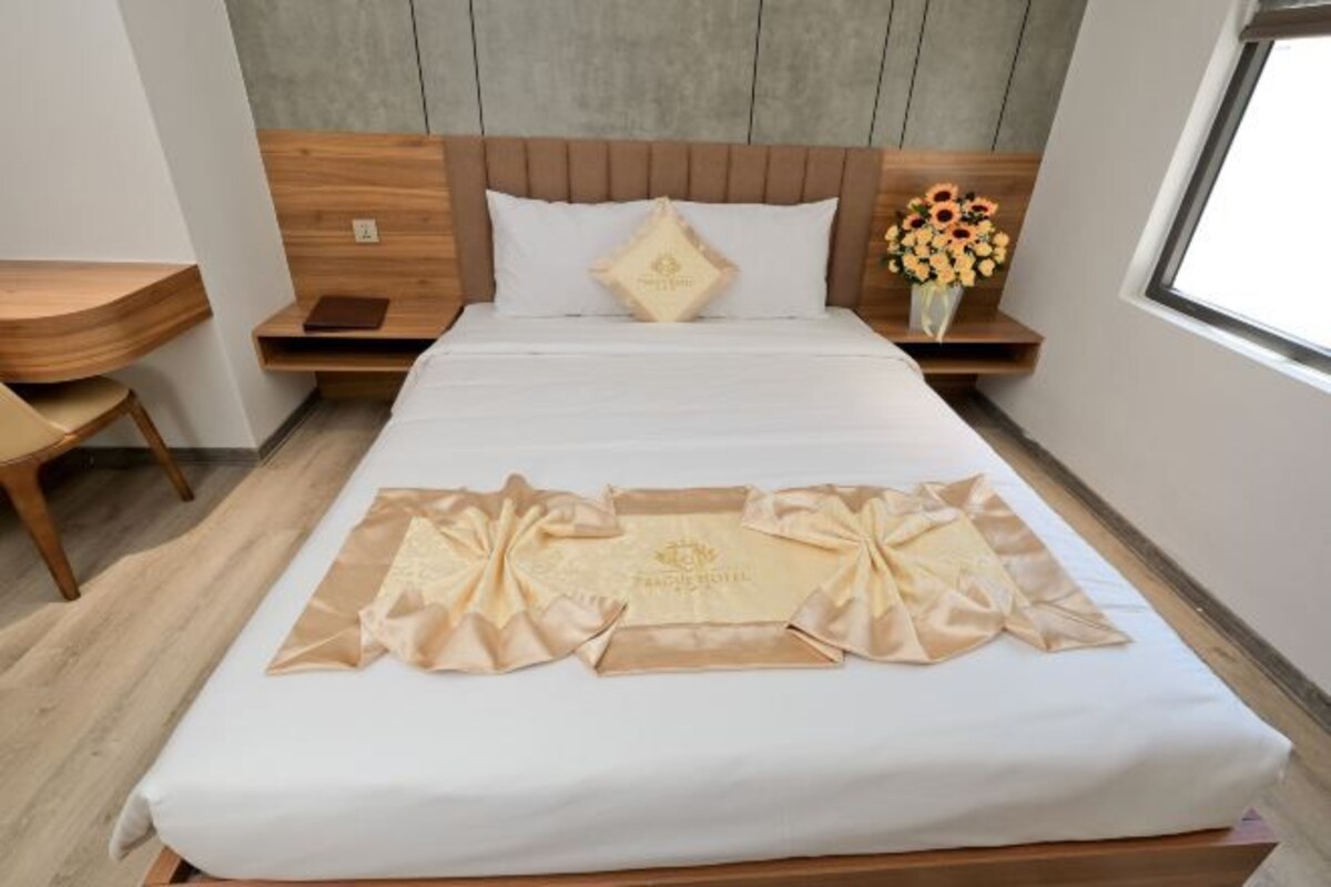 A neatly made bed with a decorative headboard, a bedside table with a book, and a vase of flowers.
