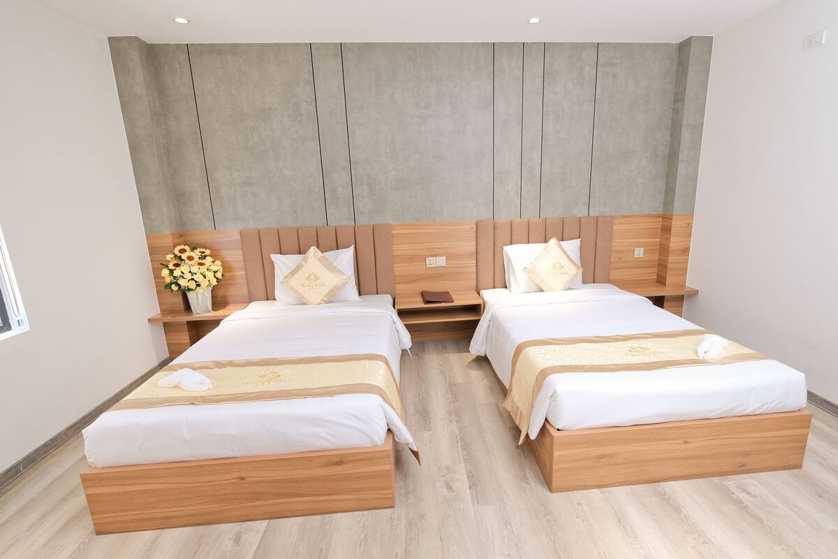 Une chambre d’hôtel avec deux lits en bois, un grand miroir et une table de chevet en bois sur laquelle est posé un vase de fleurs.