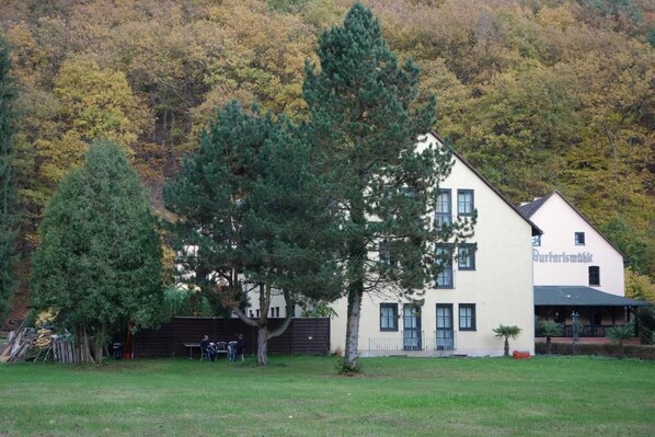 A two-story building with a sign reading "Burghofsmühle". There is a large tree in front of the building, and a grassy area in the foreground. - Landhotel Burkartsmühle (Hofheim am Taunus)
