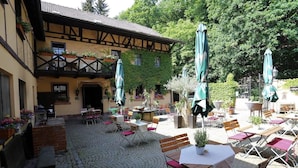 An outdoor café area with tables and chairs, surrounded by a cobblestone courtyard and a building with a timber-framed structure. - Landhotel Burkartsmühle (Hofheim am Taunus)