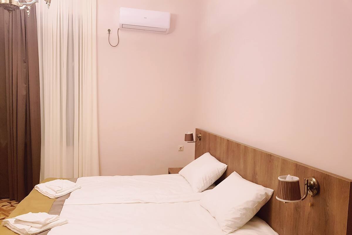 A hotel room with a bed, a bedside lamp, a telephone, and a wall-mounted air conditioner.