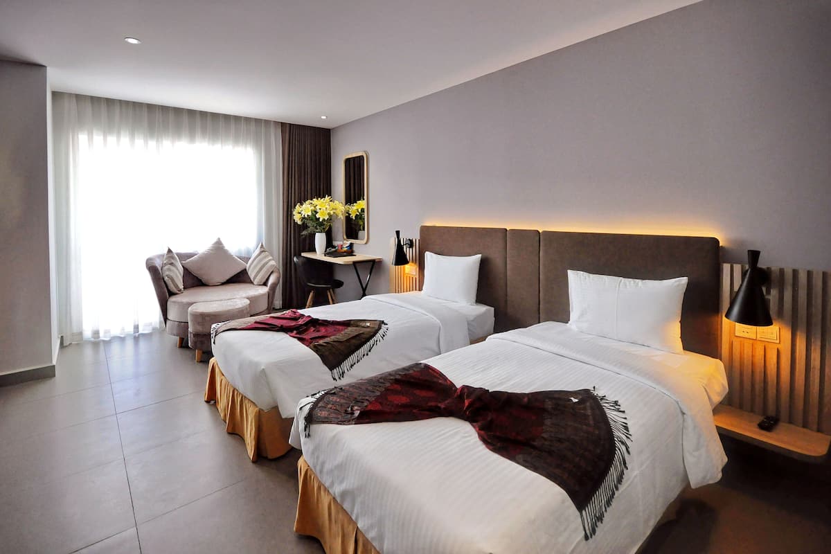 Une chambre d’hôtel avec deux lits, un canapé, un bureau et une grande fenêtre avec des rideaux.