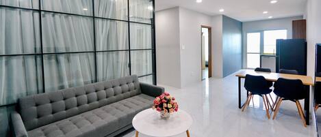 A modern living room with a grey sofa, a white coffee table with a flower vase, and a dining area with a table and chairs.