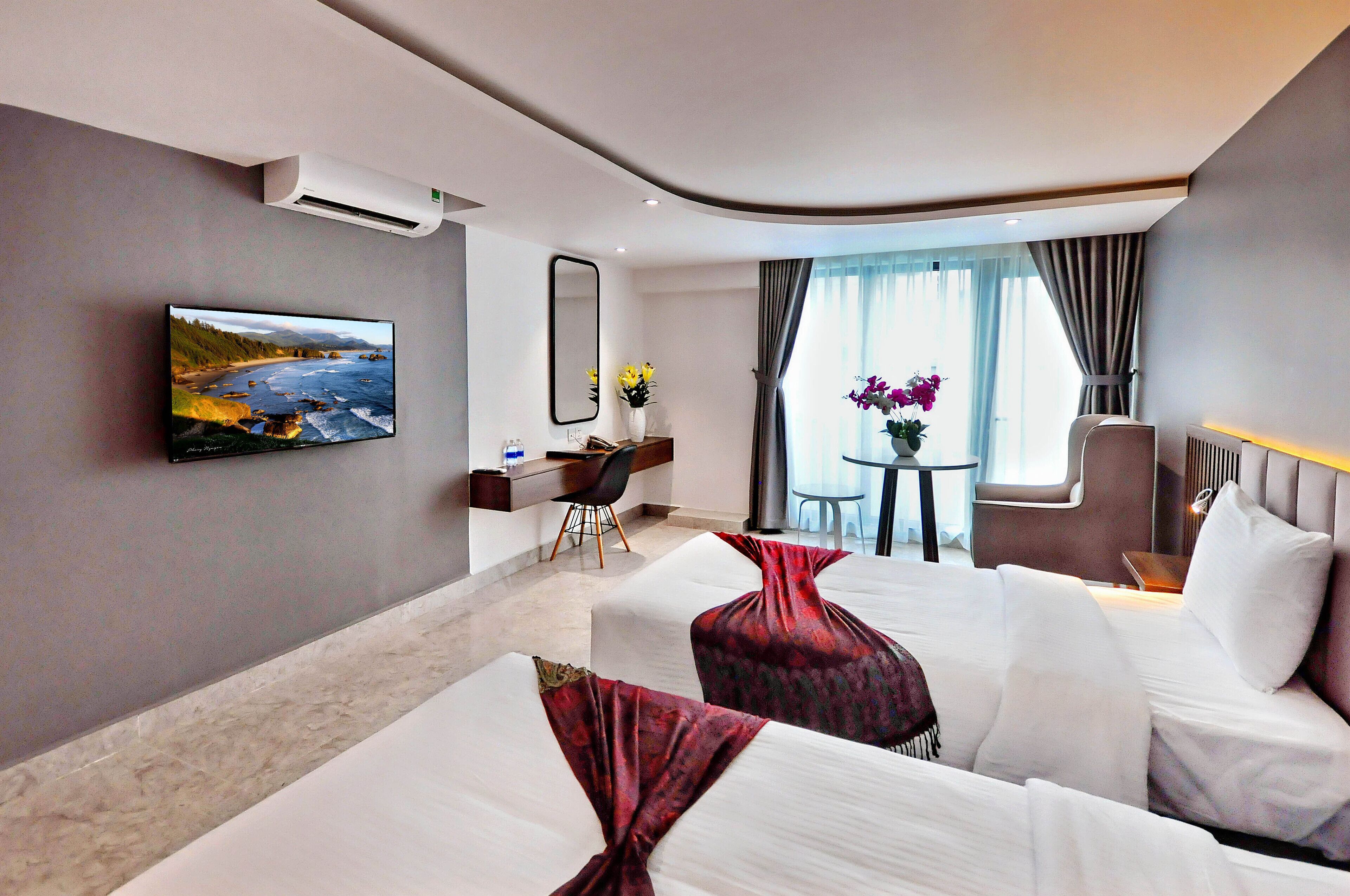 A hotel room with a large bed, a desk with a chair, a TV, and a view of the outdoors.
