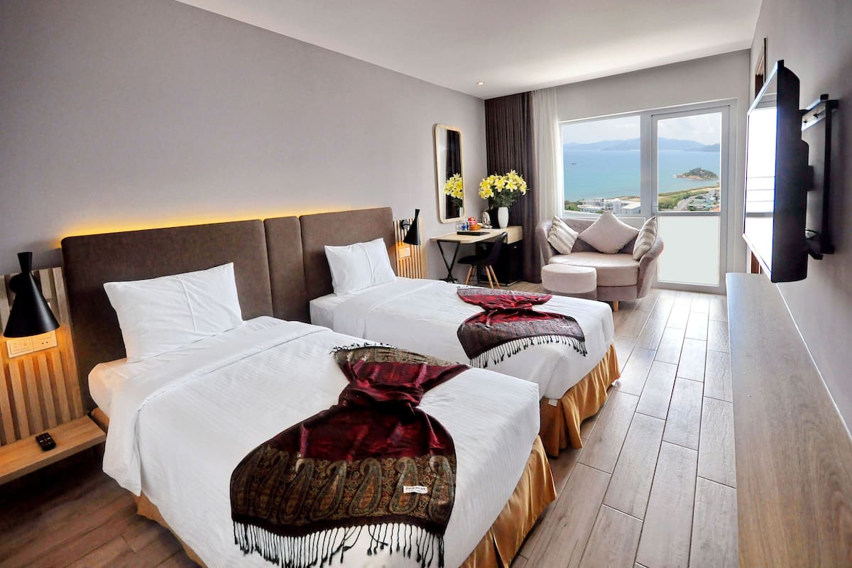 Une chambre d’hôtel avec deux lits, un bureau, une chaise et une grande fenêtre donnant sur la mer.