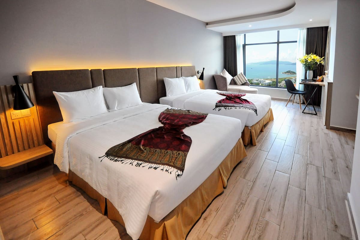 Une chambre d’hôtel avec deux lits, un bureau, une chaise et une grande fenêtre donnant sur un beau paysage.