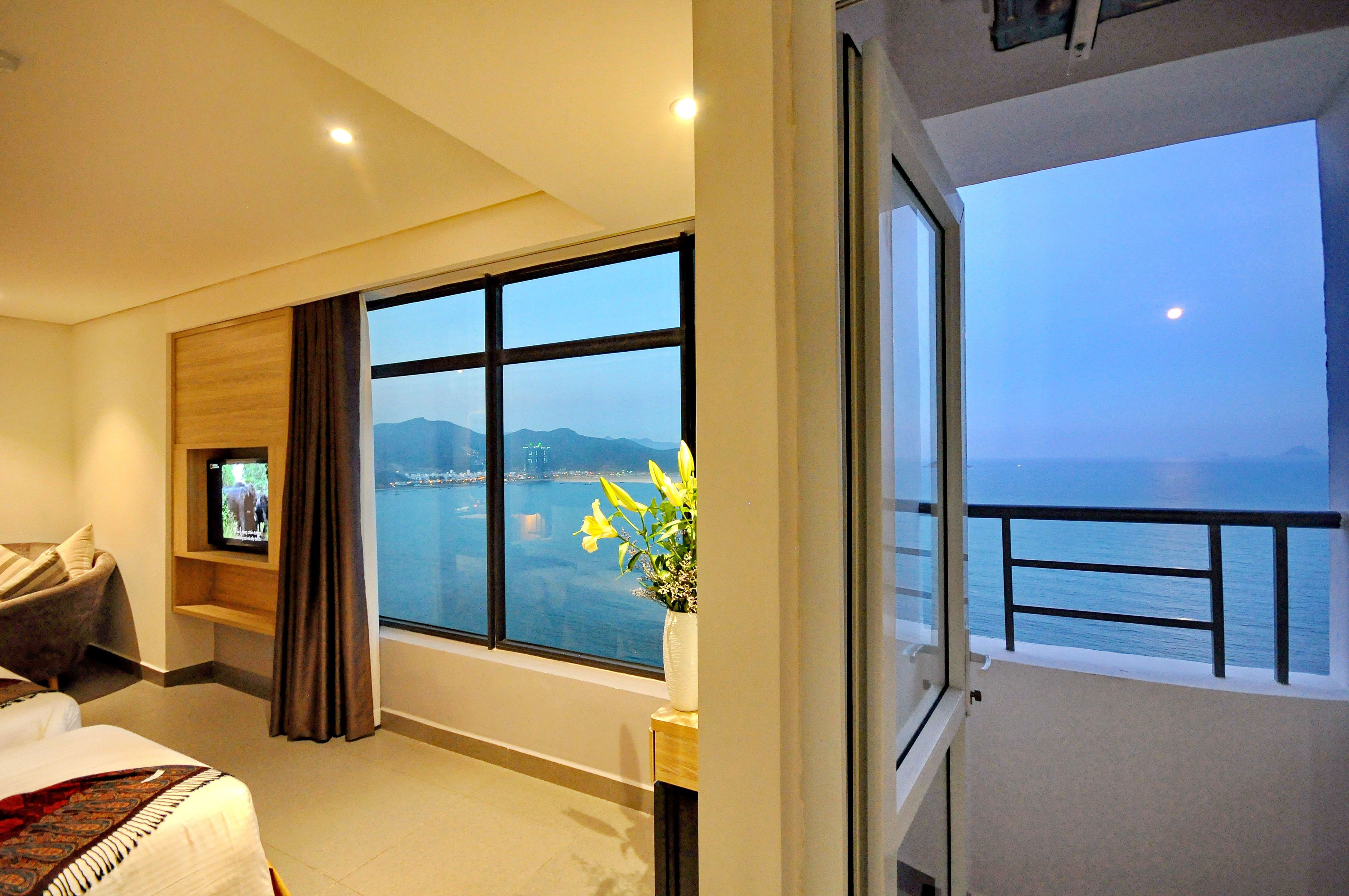 A hotel room with a large window offering a view of the sea and mountains.