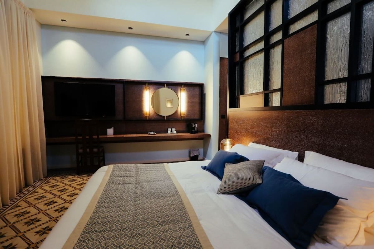 Une chambre d’hôtel avec un grand lit, un bureau doté d’un téléviseur à écran plat, un miroir et une fenêtre donnant sur l’extérieur.