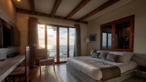 Een slaapkamer met een groot bed, een bureau en een stoel, met uitzicht op zee door een glazen deur.