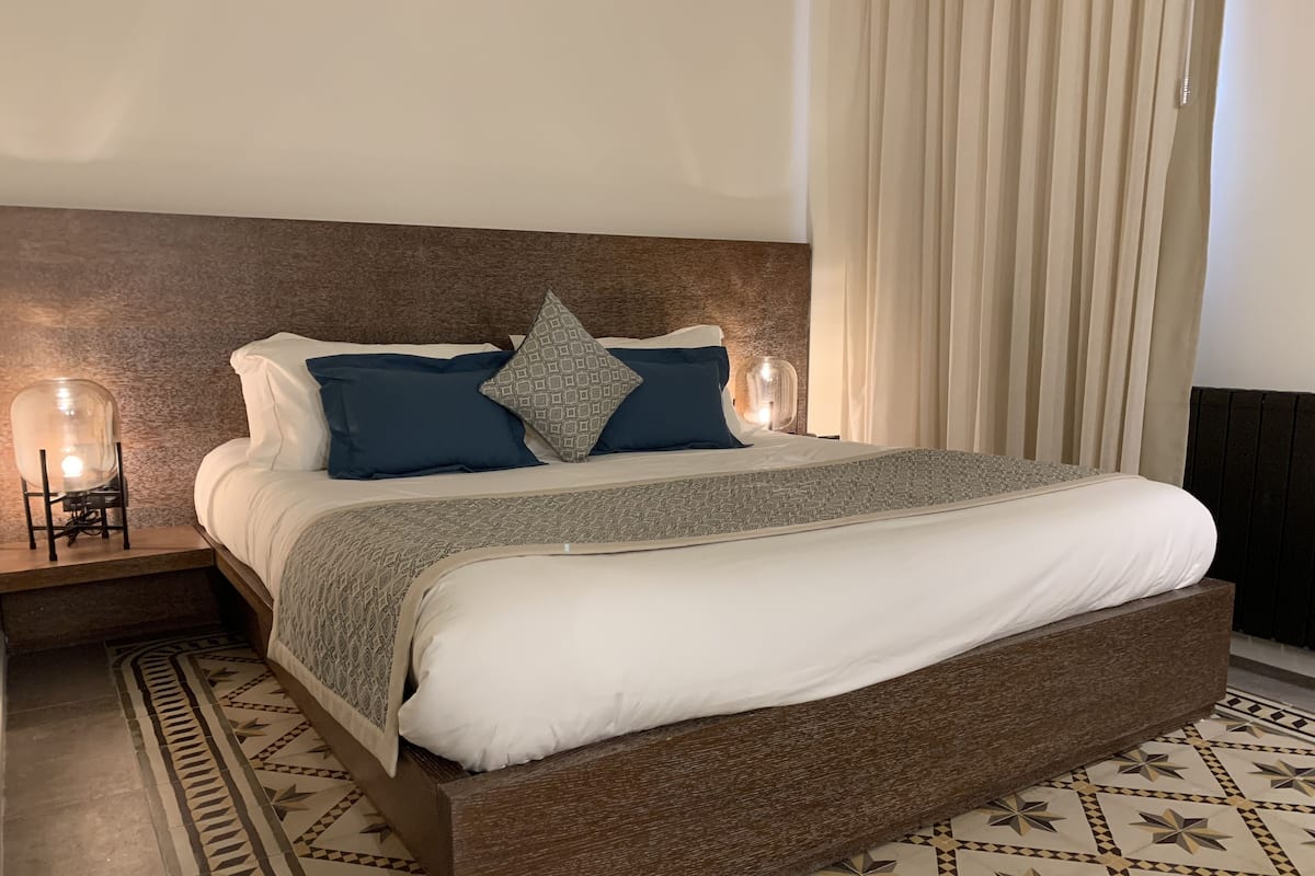 Un lit bien fait, recouvert d’une couvre-lit à motifs, avec deux oreillers et une table de chevet sur laquelle se trouve une lampe.