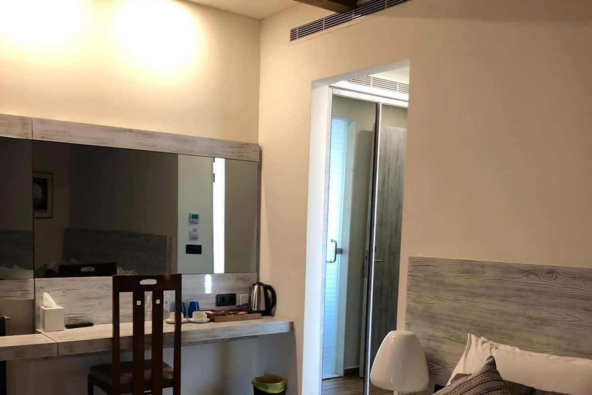 Une chambre d’hôtel moderne, dotée d’un grand lit, d’un bureau avec une chaise, d’un miroir et d’une table de chevet avec une lampe.