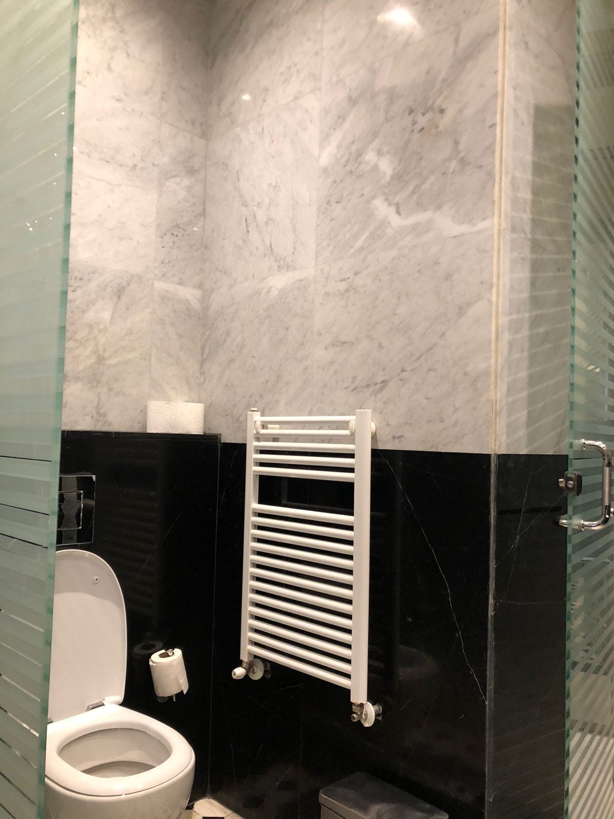 A bathroom with a white toilet, a glass shower enclosure, and a black tiled wall.