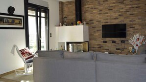 A living room with a grey sofa, a white chair, a fireplace, and a TV mounted on the wall. - Bright Cozy vintage apartment (Athina)