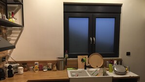 A kitchen with wooden cabinets, a window with frosted glass, a sink, and various kitchen items on the countertop. - Bright Cozy vintage apartment (Athina)