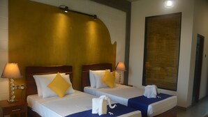 A hotel room with two beds, each with a wooden headboard, white bedding, and yellow pillows. There are lamps on either side of the beds, and a towel is placed on the floor between them. - Royal Tusker Udawalawa (Udawalawa)