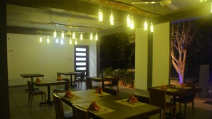 A restaurant with tables set for dining, hanging lights, and a view of the outdoors. - Royal Tusker Udawalawa (Udawalawa)