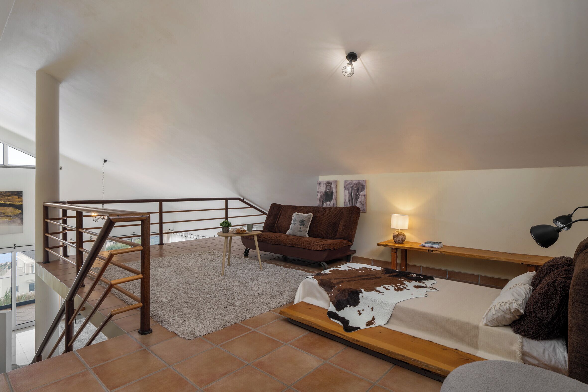 Um amplo quarto no estilo loft, com uma cama grande, um sofá de couro marrom, um banco de madeira, uma mesa pequena e uma escada.